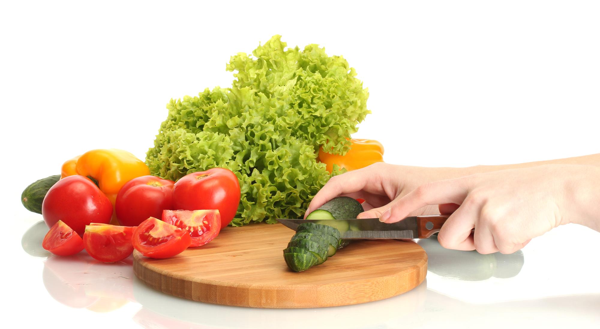 Manos cortando verduras sobre tabla en cocina moderna