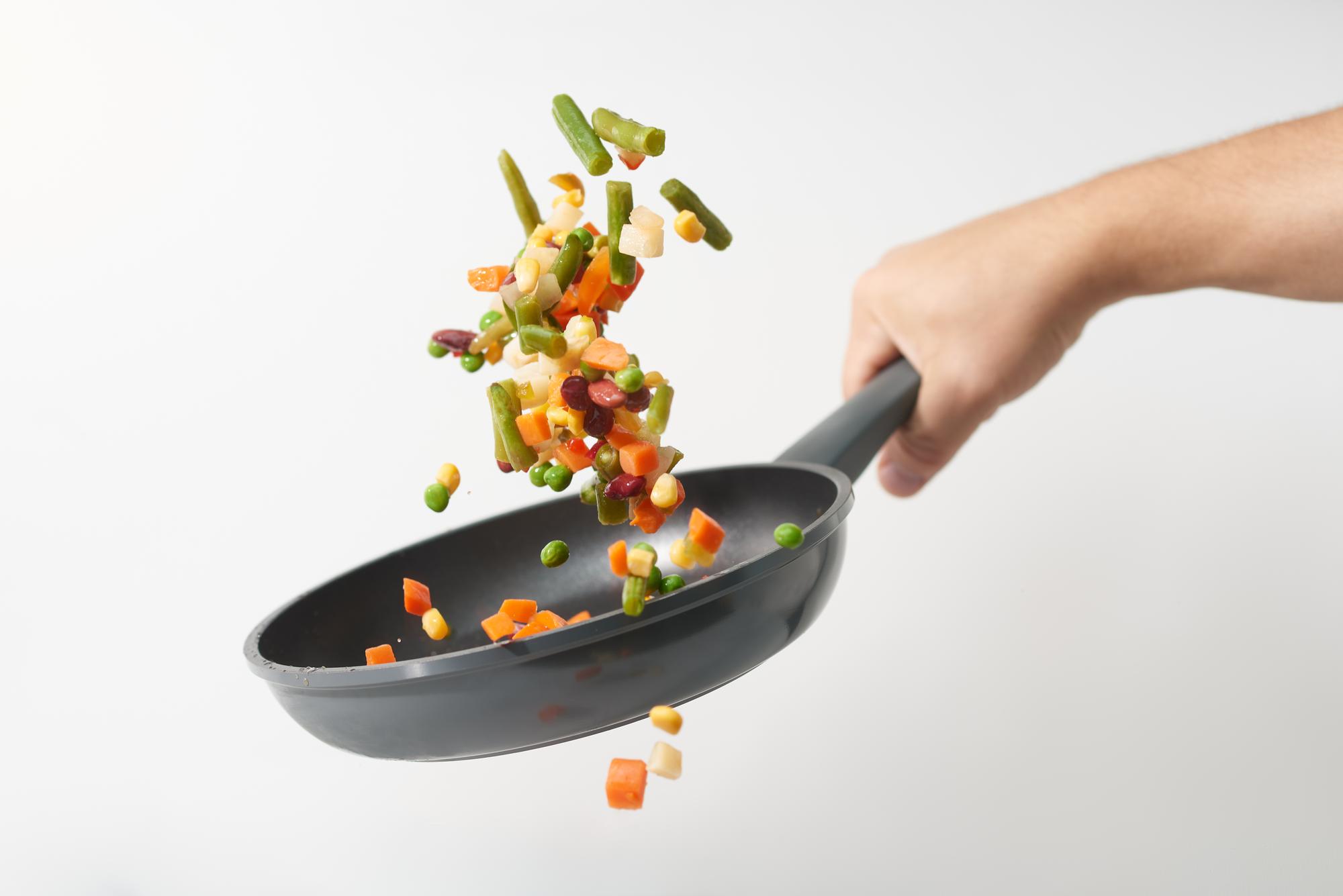Detalle de manos salteando verduras en sartén